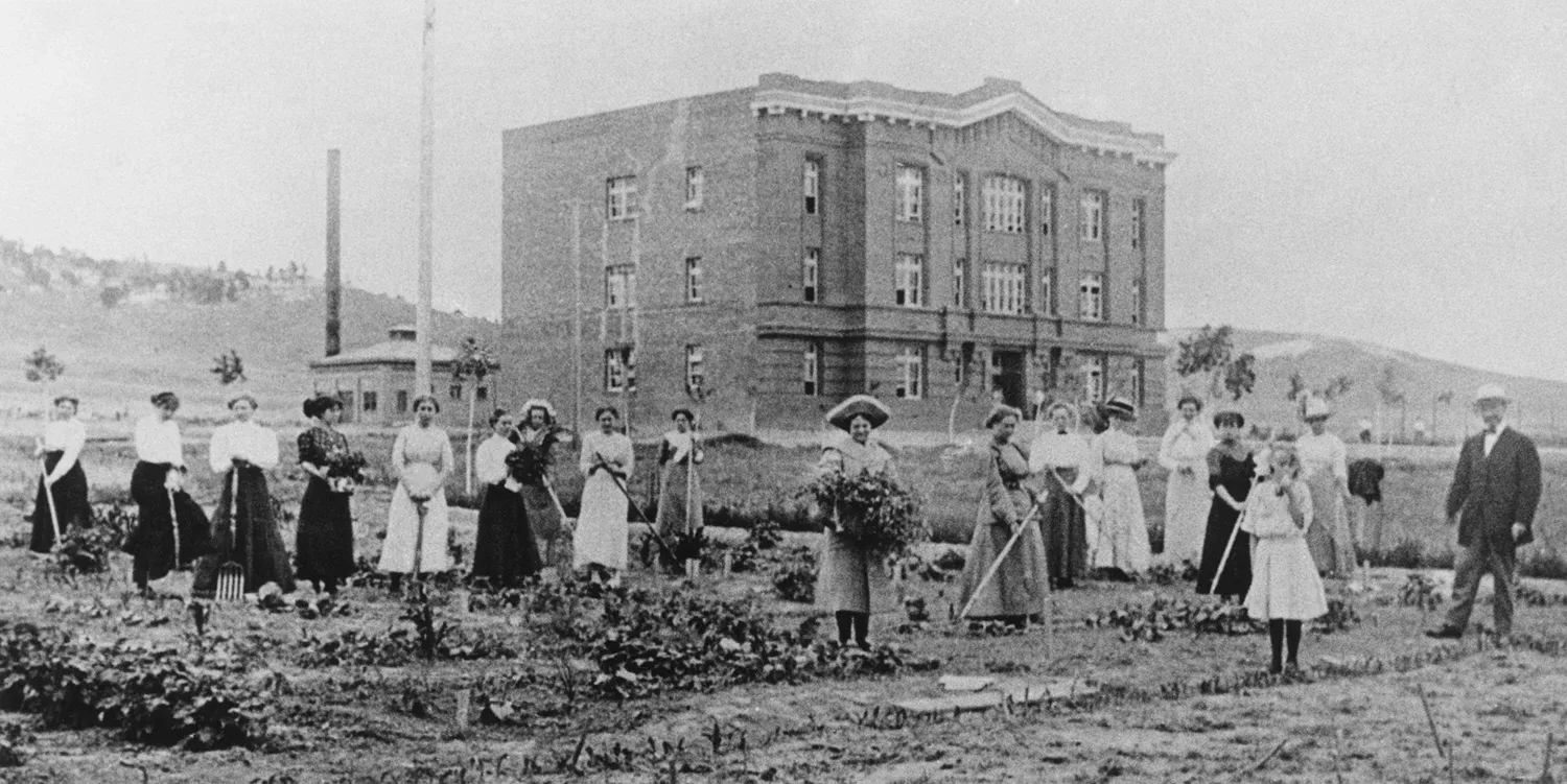 Group of students working in a garden with a three story academic building in the background